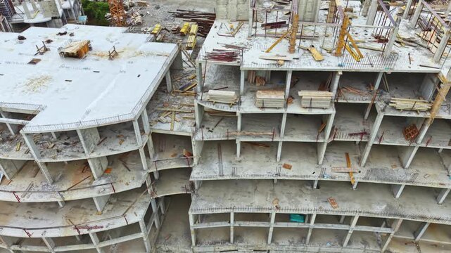 Aerial view concrete building under construction showing exposed floors, curved facade, rebar and formwork temporary supports and materials scattered