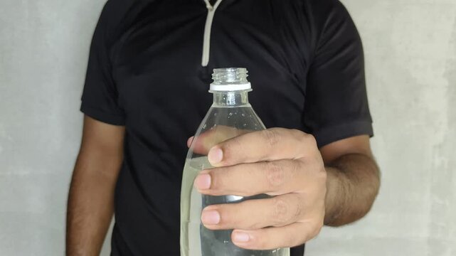A thirsty person holding a large plastic water bottle, opening the cap, and then showing the bottle toward the camera. Drinking water scarcity, shortage and microplastic contamination concept.