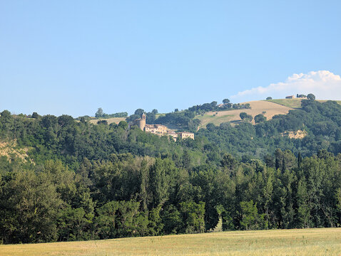 Borgo antico immerso nel verde, con campi e colline circostanti sotto cielo limpido. Atmosfera rurale, tranquilla e luminosa