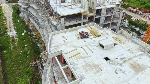 Workers are building a large structure in an urban area. Concrete and steel are visible on the site. The building is still under development and shows unfinished areas.