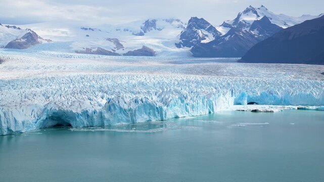 Majestic Perito Moreno Glacier in Argentina with massive blue ice walls and high snow-capped mountains under a bright sky, a stunning view of Patagonian nature