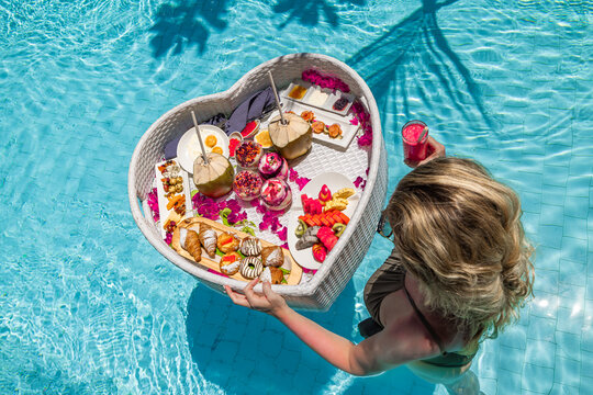 Stunning luxury resort swimming pool romantic floating breakfast heart shaped tray sensual long hair woman enjoying tropical honeymoon vacation. Dreamy summer holiday paradise escape, exotic getaway