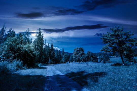 mysterious view of a country road in carpathian mountains for travel at night. road journey through forested countryside summer scenery. full moon over forest on the background hill. sky with clouds