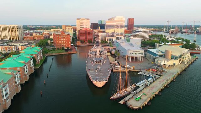 Norfolk, Virginia, scenic 4K aerial video establishing the historic battleship USS Wisconsin and the Nauticus museum along the downtown city waterfront during a vibrant golden hour sunset.