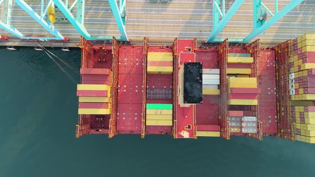 Portsmouth, Virginia, striking 4K top-down aerial video tracking sideways over a massive MSC cargo container ship docked under teal gantry cranes at the Virginia International Gateway (VIG) terminal.