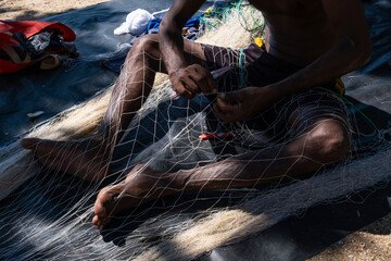 Local Sri Lankan fisherman weaving and repairing nylon fishing net on a sandy beach. © Сергей Дудиков
