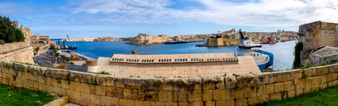 View across the Grand Harbor towards Fort St Angelo and historic fortifications under blue sky in Valletta