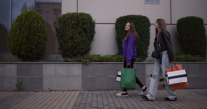 Two Teenage Girls Enjoy a Shopping Spree, Walking Down the Street with Shopping Bags and Sharing a Laugh