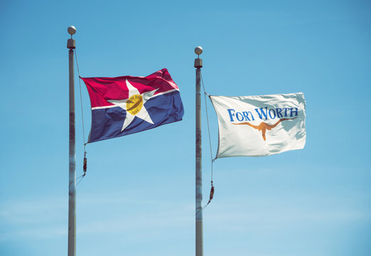 City of Dallas and Fort Worth, Texas, flags waving in the wind on flagpoles. Blue sky background. 