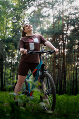 Naklejka premium Woman Standing With Bicycle Looking Skyward Amid Tall Pines, Uplifted Expression, Sunlight Filtering Through Canopy, Sense Of Freedom And Joyful Pause