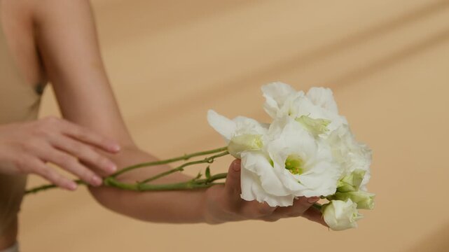 Close-up selective focus view of female hand holding small bouquet of white lisianthus flowers against beige background