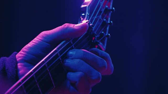 A close-up of a musician's hand playing a powerful chord on the neck of an electric guitar. Live rock concert. Moody green lighting highlights the fingers on the frets