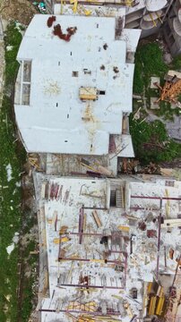 Workers are constructing a multi-storey building at a construction site. Various materials such as wood, metal, and concrete are scattered throughout the area, showing active building progress.