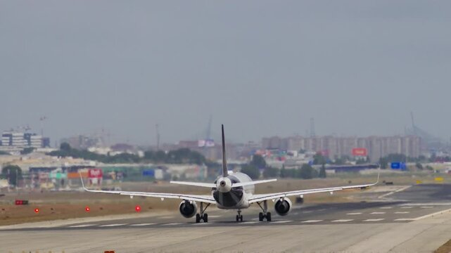 Commercial narrow body jet in rotation phase during takeoff run, rear view, red edge lights and hazy city skyline visible in background