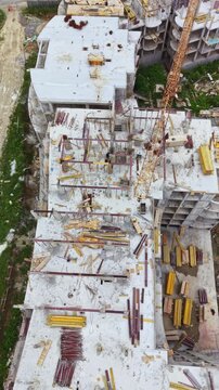 A construction site is busy with workers and cranes. Materials are scattered around the surface, showing the ongoing work to build a multi-storey structure during daylight hours.