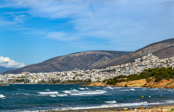 Coastal view of the Athens Riviera from Kavouri with waves and cityscape under blue sky, Greece