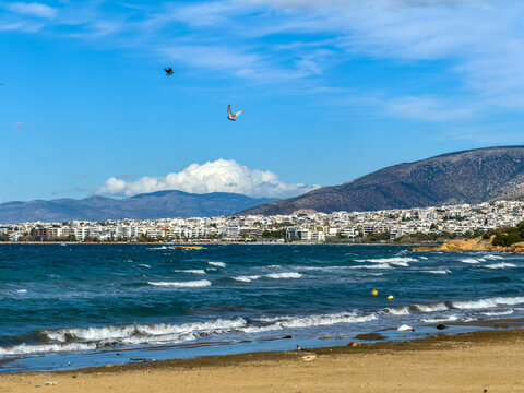 Coastal view of the Athens Riviera from Kavouri with waves and cityscape under blue sky, Greece