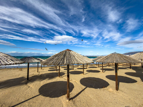 Rows of straw beach umbrellas on sandy shore by the Aegean Sea in Vouliagmeni, Attica, Greece