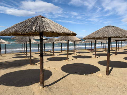 Rows of straw beach umbrellas on sandy shore by the Aegean Sea in Vouliagmeni, Attica, Greece