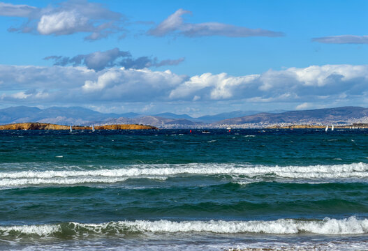 Aegean sea waves and sailboats near Vouliagmeni coast Attica Greece under bright clouds and blue sky