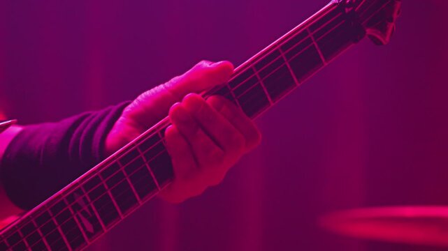 Musician plays heavy metal riff on electric guitar. Intense green stage light creates energetic mood during live performance. Close up focus on hand and fretboard. Ideal for music concepts