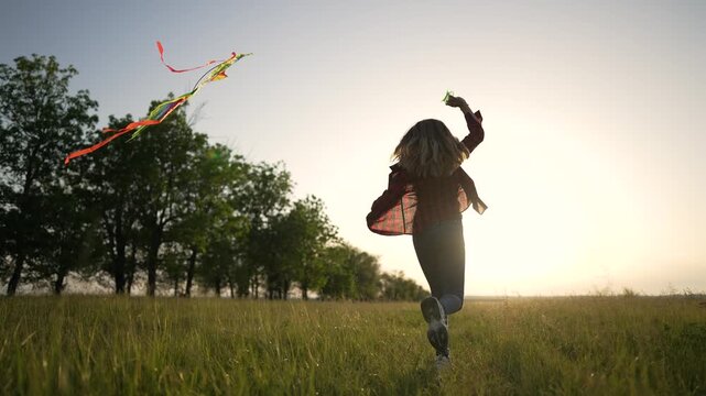 Girl running with toy airplane in sunset field. Child plays with plane in green meadow at golden hour. Kid runs through tall grass holding airplane toy. Happy childhood dream of flying in nature.