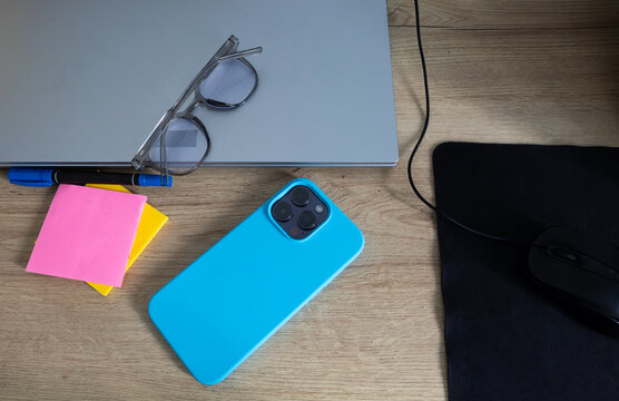 Top view of a laptop, mobile phone, and glasses placed on a desk. Concept of work, study, technology, productivity, and a modern office environment
