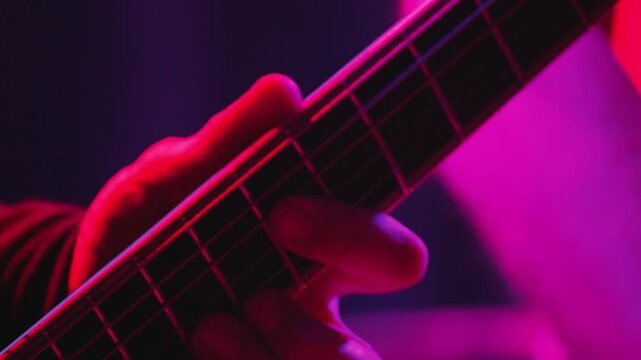 Close up of guitarists hand playing heavy metal music on electric guitar. Fingers press strings on fretboard during live performance
