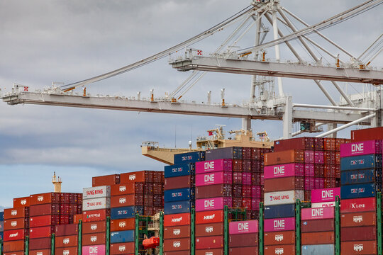 Gantry cranes operating above ONE and Hapag‑Lloyd cargo containers at an industrial shipping terminal in Oakland, California