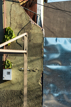 Weathered urban wall contrasts metal panel, foliage, and angular street structure