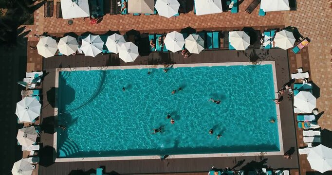 Aerial top down view of a rectangular blue swimming pool surrounded by white umbrellas and sun loungers at a resort