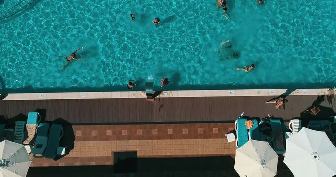 Aerial top down view of a rectangular blue swimming pool surrounded by white umbrellas and sun loungers at a resort