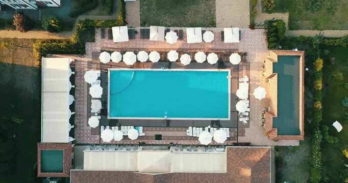 Aerial top down view of a rectangular blue swimming pool surrounded by white umbrellas and sun loungers at a resort