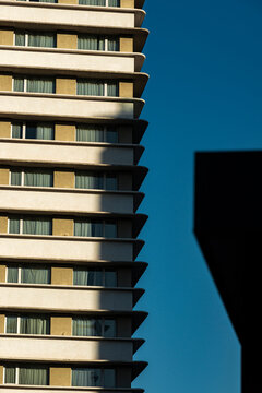 Sculptural hotel facade recedes in stacked bands with bold shadow against blue sky