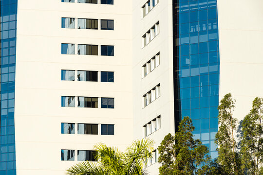 Layered office complex combines blue glass grids with white facade and greenery