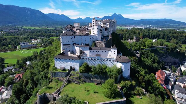 Hohensalzburg Fortress Salzburg Austria Aerial 4K. Drone cinematic orbit flyby of white medieval castle with majestic mountains. Scenic old town city center overview and blue church domes, copy space 
