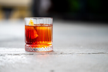 A classic Negroni cocktail with an orange peel garnish is served in a crystal rocks glass on a rustic concrete surface, close-up shot with a shallow depth of field. © pavel siamionov