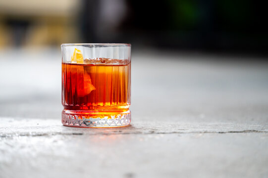 A classic Negroni cocktail with an orange peel garnish is served in a crystal rocks glass on a rustic concrete surface, close-up shot with a shallow depth of field.