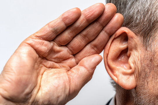 An older man holds his hand near his ear. Space for text.