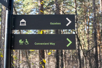 Fototapeta premium Directional signpost displays arrows for gazebos and convenient way, surrounded by trees and natural foliage in a wooded area
