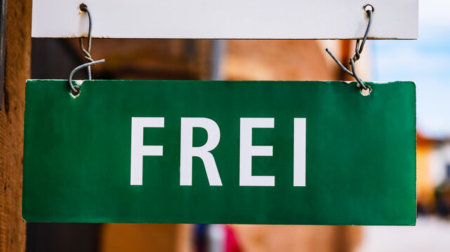 Sign hanging that shows the word frei in a town with bright sky and buildings nearby
