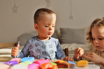 Naklejka premium Two children are engaged in play with colorful clay in a bright indoor area during the morning. They focus on their creative activity at a table