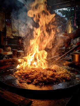 Sri Lankan street vendor cooking kottu roti on a large iron griddle with dramatic fire sparks flying.