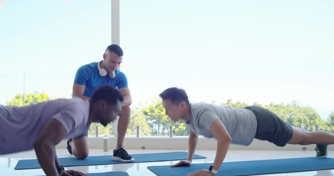 Coach timing reps, supervising two men tapping hands and doing pushups on blue mats in studio