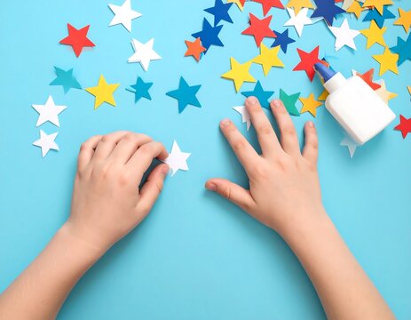 Child's hands crafting with colorful star cutouts and a glue bottle on a vibrant blue surface