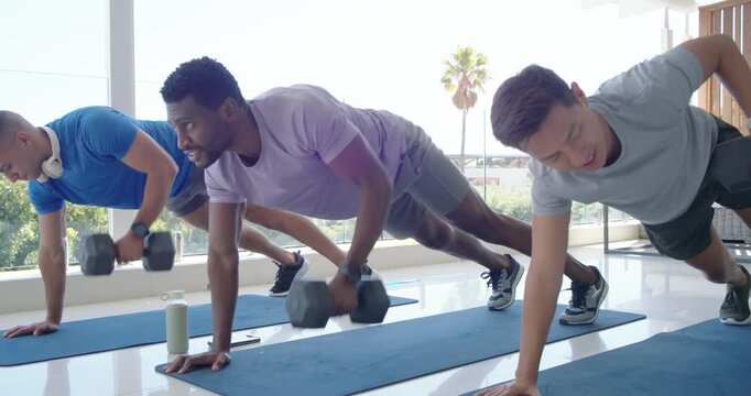 Three men starting plank rows on blue mats by glass wall, using hex dumbbells, training core