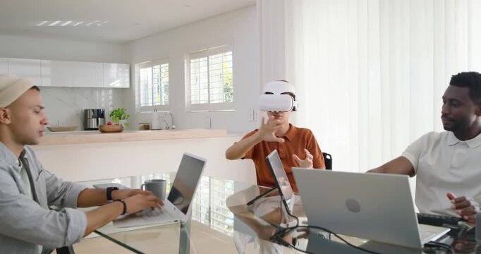 Diverse male coworkers watching Asian man putting on white VR headset during demo at kitchen table