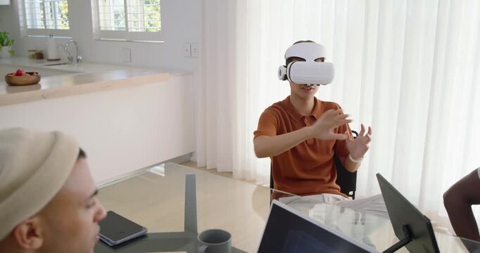 Mid-adult Asian man in rust polo during demo, picking up white VR headset, gesturing in kitchen