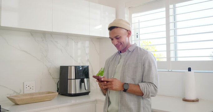 Adult man reading message on smartphone standing by kitchen counter, replying beside air fryer