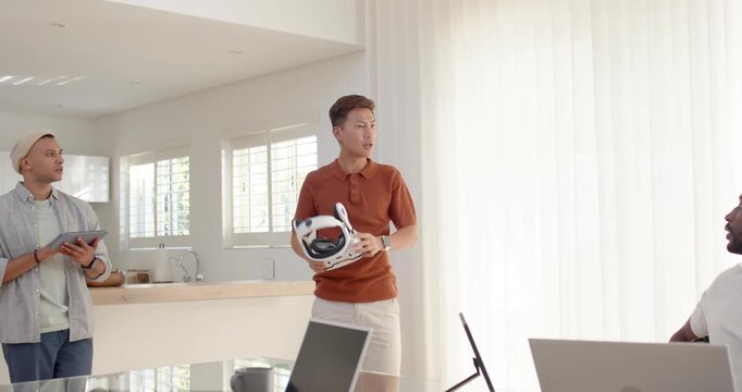 Diverse males watching Asian presenter bringing white VR headset for demo in kitchen, copy space